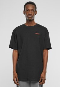 Sort bomulds t-shirt med korte ærmer, løs pasform, med et lille rødt broderet logo på brystet. Glat tekstur.
