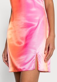 Vestido de satén con un degradado de naranja a rosa, que presenta una abertura alta en el muslo y una textura suave y brillante. Costuras acentuadas resaltan el diseño.