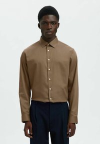 Πουκάμισο με μακριά μανίκια από καφέ ύφασμα με ομαλή υφή, διαθέτει μυτερό γιακά και μπροστινό κούμπωμα με κουμπιά. Κλασικός σχεδιασμός με διακριτική γυαλάδα.