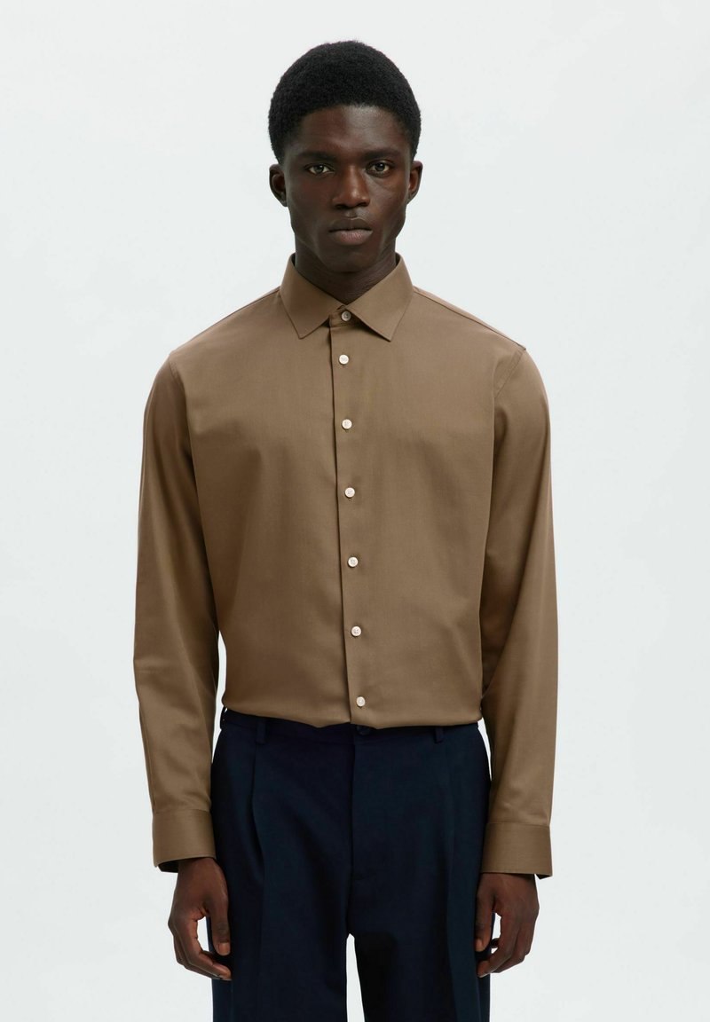 Πουκάμισο με μακριά μανίκια από καφέ ύφασμα με ομαλή υφή, διαθέτει μυτερό γιακά και μπροστινό κούμπωμα με κουμπιά. Κλασικός σχεδιασμός με διακριτική γυαλάδα.