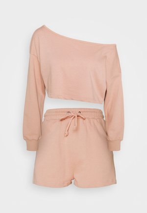 Ensemble d’intérieur deux pièces couleur pêche, composé d’un crop top asymétrique à manches longues et d’un short à taille coulissée par un cordon.