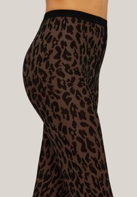 Leggings in stampa leopardata realizzati in tessuto trasparente marrone, con una vita elastica nera. Il motivo è composto da macchie marroni scure e nere.