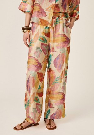 Mujer que lleva pantalones sueltos y ligeros con un patrón abstracto de hojas multicolor, combinados con una blusa a juego y sandalias marrones con tachuelas.