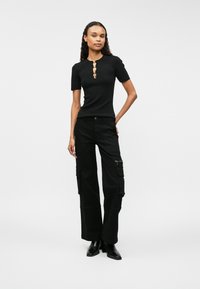 Svart kortermet topp med rund hals og fem gullknapper. Svart cargo bukser med sidelommer og en glidelåsdetalj ved hoften.