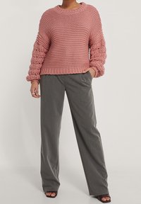 Rosa stickad tröja med strukturerade, voluminösa ärmar; kombinerad med lösa grå byxor och svarta öppna klackar.