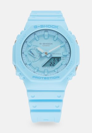 Montre G-SHOCK bleu clair avec un boîtier rond en résine, affichage numérique et analogique, bracelet en caoutchouc texturé et accents argentés. Étanche jusqu'à 20 bars.
