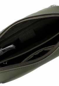 Rohelise sünteetilise õlakoti sisemus, millel on sile tekstuur, mitu lukuga taskut ja brändi silt.