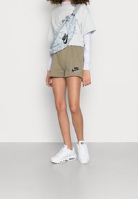 Světle modrá košile s krátkým rukávem, khaki šortky s logem, vzorovaný ledvinkou a bílé tenisky s viditelným vzduchovým polstrováním.