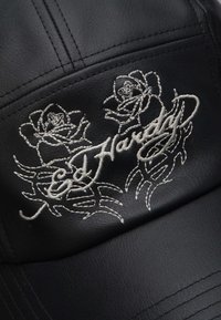 Cappello in pelle nera con rose ricamate bianche e il nome "Ed Hardy." Particolari dettagli di cucitura arricchiscono il design.
