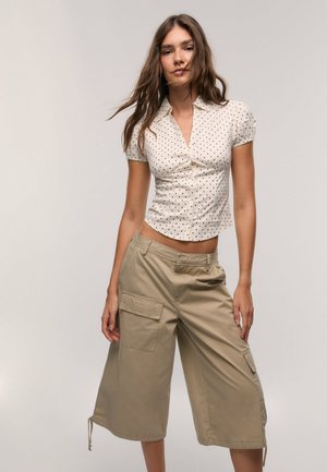 Polka-dotted, short-sleeve, fitted blouse in cream; paired with beige, knee-length cargo pants featuring side pockets and drawstring hems.