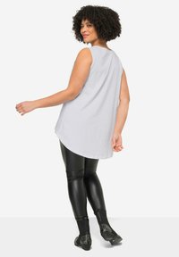 Top sin mangas de color gris claro con un dobladillo redondeado, combinado con leggings de imitación cuero negro y botas negras con tachuelas hasta el tobillo.