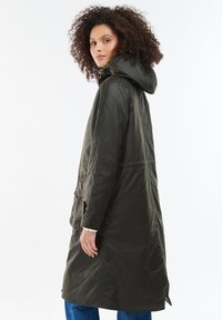 Lungo cappotto verde oliva con cappuccio, dotato di chiusura con bottoni e zip, due tasche frontali e una vestibilità morbida. Tessuto liscio e resistente all'acqua.