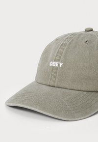 Olive green cotton cap with a curved brim and white "OBEY" embroidered on the front. Soft texture with stitching detail along the brim.