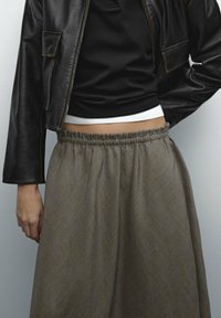 Ruskea ruudullinen hame, jossa on joustava vyötärö, yhdistetty mustaan istuvaan yläosaan ja lyhythihaiseen nahkatakkiin. Hameessa on teksturoitu pinta.