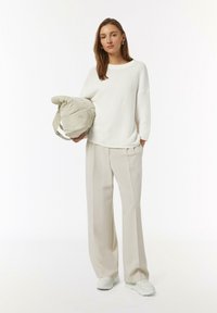 Oversized white knit sweater paired with beige wide-leg trousers and white sneakers. A padded beige bag is held in one hand.