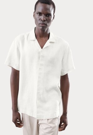 Camisa de lino blanca de manga corta con cuello, que presenta un cierre frontal con botones y un corte relajado. Textura suave, diseño casual.