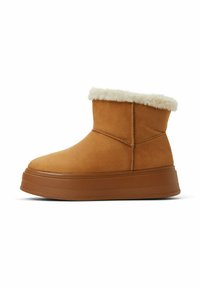 Botas de tobillo de ante color canela con un ribete de piel sintética blanca, que presentan una gruesa suela de plataforma marrón, detalles de costura y un diseño minimalista.