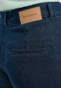 Donkerblauwe spijkerbroek van denim met een leren label met de tekst "hessnatur," voorzien van een achterzak en subtiele stikseldetails.
