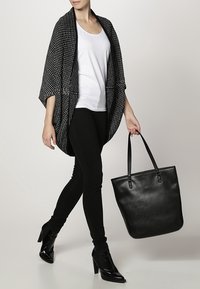 Mustekalasilla kuvioitu kimono, valkoisen puseron päällä, yhdistettynä mustiin tiukkoihin farkkuihin ja mustiin korkokenkiin, pitelee mustaa kassi.