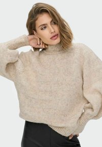 Ümarav beige sviiter kõrge kaeluse, soonikute mansettide ja pehme, tekstureeritud kangaga. Üks suurus suurem sobivus, minimaalne muster, stiilitud mustade pükstega.