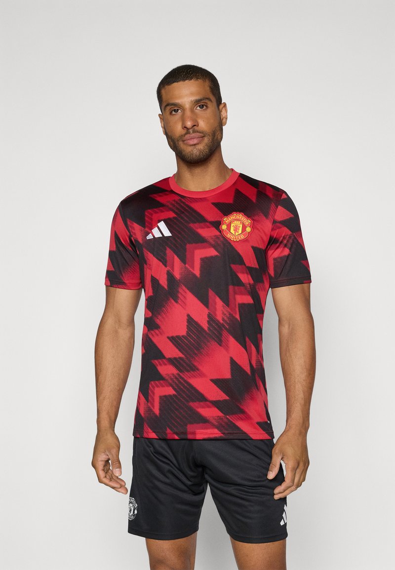 Roter und schwarzer Fußballtrikot mit Zickzackmuster, rundem Ausschnitt und Manchester United-Emblem. Schwarze Shorts mit Logo.