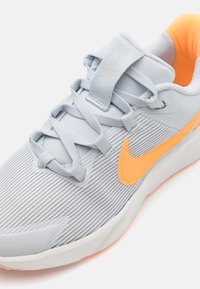 Baskets de sport gris clair avec une tige en maille texturée, des accents orange et un col rembourré, dotées de lacets plats et d'une semelle en caoutchouc.