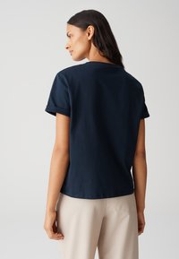 T-shirt in cotone blu navy con maniche corte arrotolate, scollatura rotonda e vestibilità rilassata, abbinata a pantaloni beige chiaro.