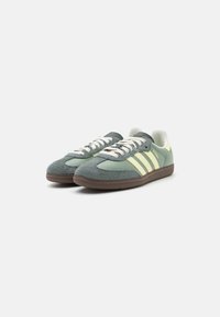 Green and yellow suede sneakers with three parallel stripes, flat laces, and a textured brown rubber sole. Rounded toe design.