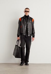 Sort læder bomberjakke med orange accenter, sort turtleneck, mørke denimbukser, sorte flade sko og en sort tote taske.