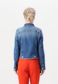 Denimjacke in Hellblau mit einem cropped Schnitt, Knopfdetails, ausgefranstem Saum und langen Ärmeln, kombiniert mit roten Hosen.