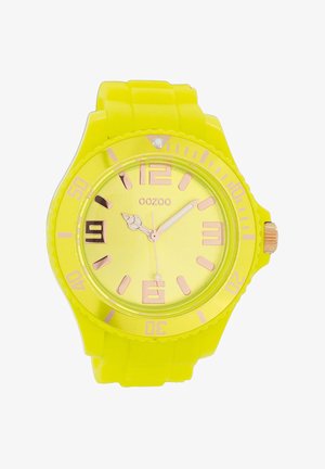 Montre en silicone jaune avec un cadran rond, des marqueurs d'heure et des aiguilles en ton doré. Présente un bracelet texturé et une couronne en métal.