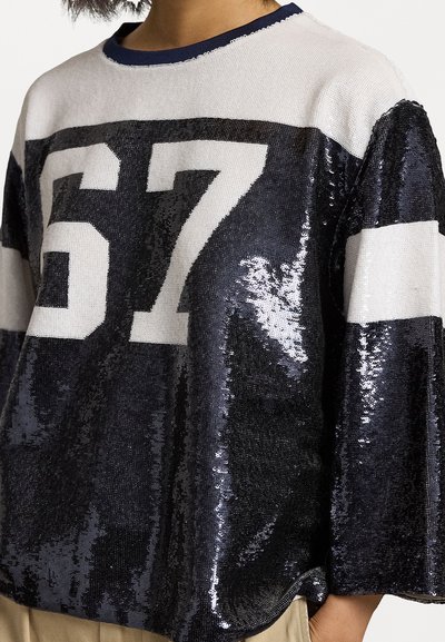 Black and silver sequined oversized sweater featuring bold white number "67," crew neckline, and wide sleeves. Textured material and sporty design.