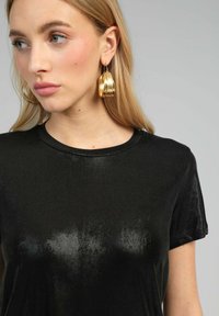 T-shirt noir à manches courtes avec une texture brillante et un col rond, accompagné de grandes boucles d'oreilles en or.