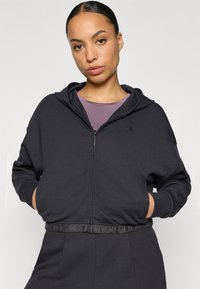 Μαύρο φούτερ με φερμουάρ από απαλό ύφασμα με υφασμένη ζώνη μέσης, που διαθέτει λογότυπο στο στήθος και επενδεδυμένη κουκούλα.