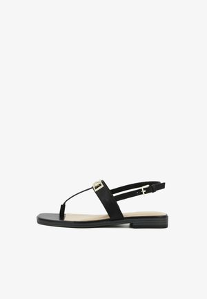 Sandalo piatto nero con cinturino a T, dettaglio fibbia dorata e cinturino regolabile alla caviglia su una soletta beige chiaro e suola nera.