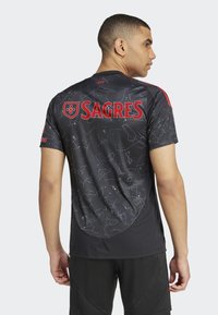 Juodas sportinis marškinėlis su raudonu užrašu "SAGRES", turintis žvaigždyno raštą ir trumpas rankoves. Lygus tekstūrinis paviršius su prigludusia forma.