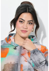 Lichtgewicht, multikleurige jas met een capuchon, met abstracte patronen in grijs, oranje, groen en blauw. Voorzijde met ritssluiting en elastische manchetten.