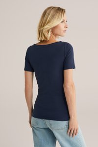 Navyblaue Kurzarmbluse mit rundem Ausschnitt, glatter Textur, figurbetonter Form und sauberer Verarbeitung. Kombiniert mit hellblauen Jeans.