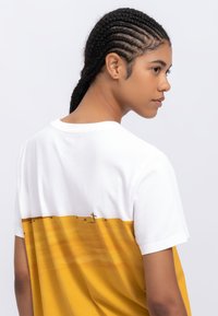 Katoenen T-shirt met een wit bovenstuk en een geel onderstuk met een landschap-print. Korte mouwen en een ronde hals.