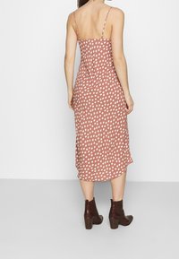 Robe midi rose poussiéreux avec des pois blancs, fines bretelles ajustables, tissu lisse et une légère fente sur le côté, associée à des bottines à talons marron.