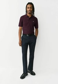 Tricou polo cărămiziu cu mâneci scurte, curea neagră, pantaloni bleumarin și pantofi negri. Prezintă un logo mic pe pieptul stâng al tricoului.