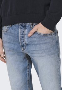 Světle modré džíny z denimu s bledým vzhledem, designem s pěti kapsami a výraznými švy. Nosit s tmavou mikinou.