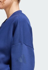 Sudadera azul con cuello acanalado, tejido texturizado y un distintivo logo de tres rayas en la manga izquierda.