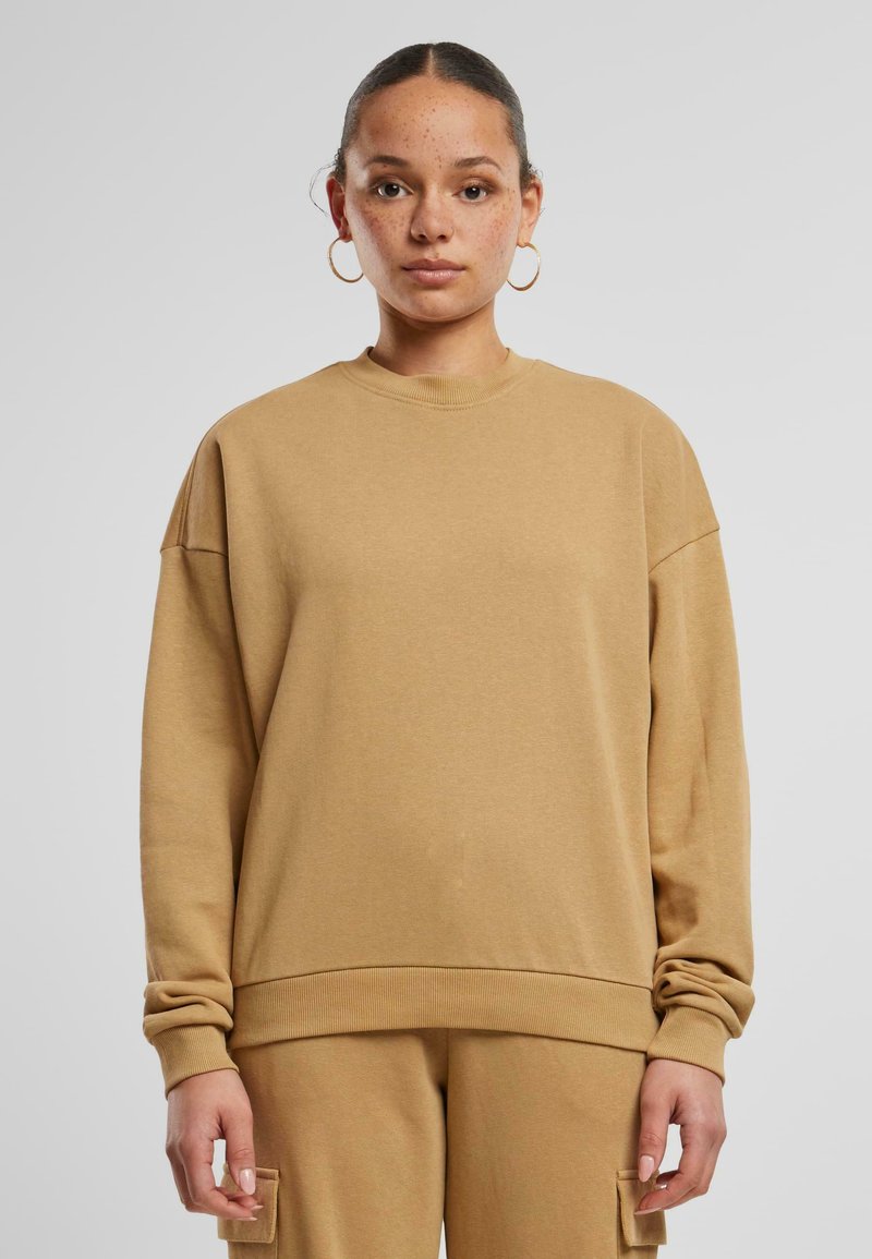 Beige übergroßer Sweatshirt aus weichem Stoff mit Rundhalsausschnitt, überschnittenen Schultern und gerippten Bündchen. Kombiniert mit passenden strukturierten Hosen.
