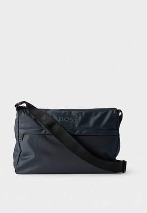 Sac besace BOSS bleu marine foncé avec fermeture zippée sur le dessus, poche avant et large bandoulière noire réglable, sur un fond uni.