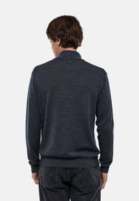 Pull en maille gris foncé avec un col et des poignets côtelés, présentant une texture lisse et une coupe ajustée. La vue de dos montre la simplicité du design.