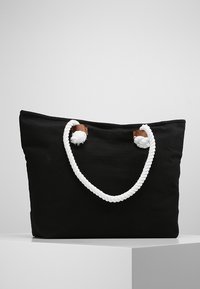 Borsa tote in canvas nera con manici in corda bianca e dettagli in pelle marrone. Design semplice e rettangolare con una texture morbida.