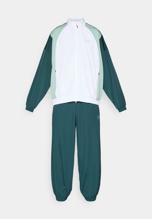 Trening format dintr-o jachetă albă cu fermoar și accente verzi, împreună cu pantaloni în culoare teal închis. Fabricat dintr-un material neted, ușor.