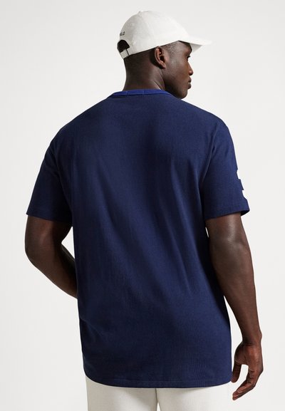 Μπλουζάκι βαμβακερό σε ναυτικό μπλε χρώμα με κοντά μανίκια και ίσιο τελείωμα, διαθέτει υφή υφάσματος και μικρή λεπτομέρεια λογότυπου στο πίσω μέρος.