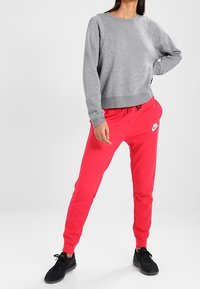 Grå sweatshirt med rund halsringning och elastisk nederkant; tillsammans med rosa sweatpants med sidofickor och en vit logotyp; svarta sneakers.